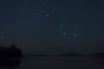 orion constellation above misty lake.