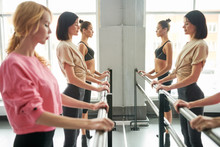 Row Of Elegant Young Women Practicing Ballet Moves Standing By Bar Against Mirror In Dance Studio