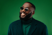 Man Portrait. Style. Handsome Afro American Guy In Green Jacket And Sun Glasses Is Looking At Camera And Smiling, On A Green Background
