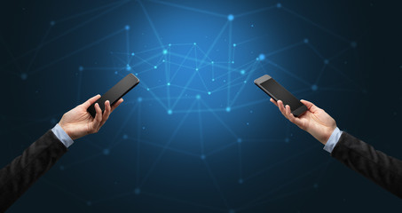 Close up of two hands holding smartphones to each other, wireless connection concept