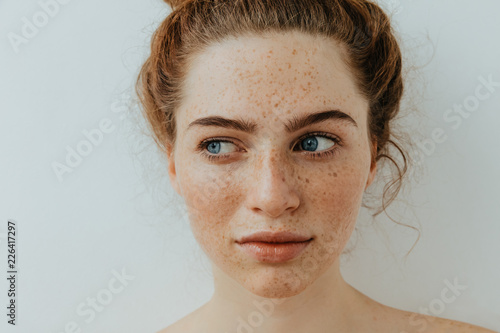 Fototapete Woman portrait. Close-up. Beautiful blue eyed girl with freckles is looking away, on a white background