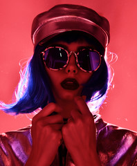 woman in street style fashion winter concept wearing gold hat cap and round sunglasses in pink neon light