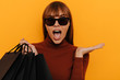 Black friday. Shopping. Woman portrait. Girl in sun glasses is holding shopping bags and looking at camera with an open mouth, on a yellow background