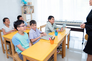 Wall Mural - Asian elementary school children smiling happily while teacher teaching in classroom