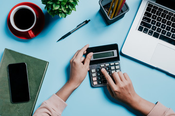 Business woman hand working with calculator,laptop and financial data on blue desk table in office.Top view with copy space,Flat lay.