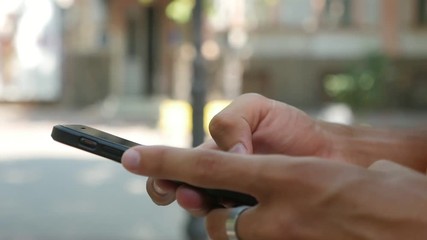  Macro shot of young male hands posting texts and browsing the net on a modern smartphone in a green street on a sunny day in summer in slow motion