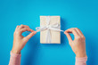© Lazy_Bear - woman's hands untie bow on gift box on blue background, top view