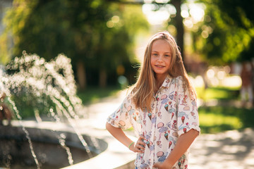 Wall Mural - blond teenage girl in a blond blouse playing with her hair on the background of a fountain