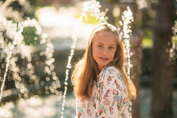 Wall Mural - blond teenage girl in a blond blouse playing with her hair on the background of a fountain