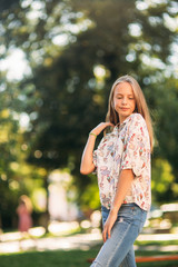 Wall Mural - blonde girl in blouse posing to photographer against the background of green tree