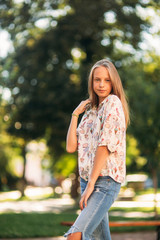 Wall Mural - blonde girl in blouse posing to photographer against the background of green tree