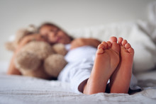 Close Up Of The Feet Of A Young Girl (kid) While She Is Sleeping On Her Bed With The Teddy Bear