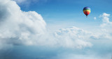 Colorful hot air balloon flying against blue cloudy sky.