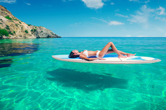 Young beautiful woman relaxing in the sea on a SUP board. The girl sunbathes on the beach of the island on vacation.