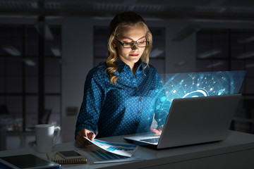 Beautiful blonde in dark office working on laptop and getting net access
