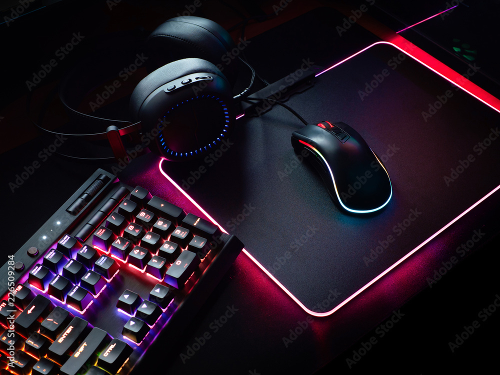 gamer workspace concept, top view a gaming gear, mouse, keyboard, joystick, headset, mobile joystick, in ear headphone and mouse pad on black table background. - obrazy, fototapety, plakaty 
