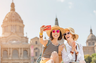 Two young happy women tourists friends hugging against the background of the National Museum of Art near the Plaza of Spain and the Montjuic Fountain in Barcelona