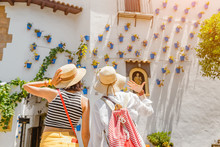 Two Girls Tourist Admiring Great View Of Flowerpots On The White Walls On Famous Flower Street In Andalusia