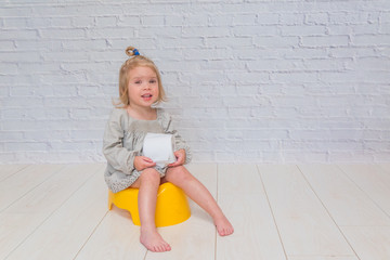 girl in a dress, a child sitting on a yellow pot with toilet paper in his hands