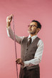 Vertical portrait of a tailor holding fabric measure, isolated on pink studio background