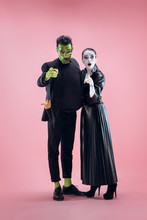 Halloween Family. Happy Couple In Halloween Costume And Makeup. Bloody Theme: The Crazy Maniak Faces On Pink Studio Background