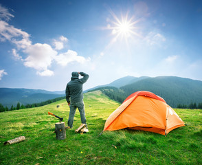 Wall Mural - man on the mountain near orange tent looks into the distance