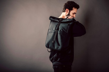 Wall Mural - Stylish young guy wearing black blank  and backpack, horizontal studio portrait