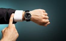 Businessman Pointing At Hand Watch On Grey
