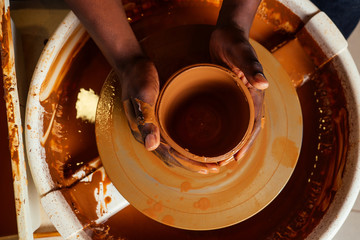 Potter's wheel dirty hands clay pot afro american potter In workshop close-up