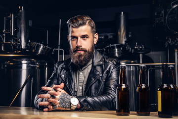 Stylish bearded biker dressed black leather jacket sitting at bar counter in indie brewery.