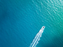 Bird's Eye Aerial Top View Of A Boat Cruising In Crystal Clear Turquoise Sea Water