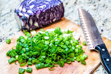 Cutting board, purple, red cabbage, scallions, sliced, cut green onion, knife in kitchen on granite countertop with nobody when cooking, preparing food, meal, salad ingredients