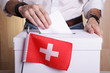 © jivimages - A Swiss citizen inserting a ballot into a ballot box. Swiss flag in front of it