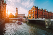 Touristic Cruise Boat On A Channel With Bridges In The Old Warehouse District Speicherstadt In Hamburg In Golden Hour Sunset Light, Germany