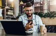 © foxyburrow - Bearded businessman sitting in cafe, talking on smart phone, working on laptop, freelancer working in coffee shop,