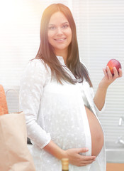 Wall Mural - young pregnant woman holding an Apple,standing in the kitchen