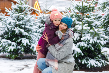 Cute little smiling kid girl and mother on christmas tree market.