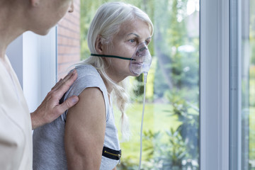 nurse supporting sick senior woman with oxygen mask in the hospital