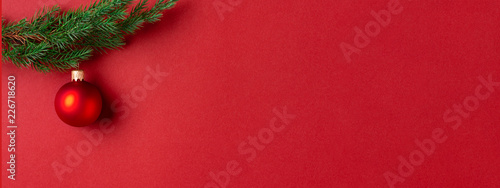 Evergreen branch with red Christmas ball on red background. New Year banner w...