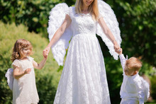 Beautiful Mother And Her Toddler Son And Daughter Wearing Angel Costumes. Cheerful Moment, Loving Family.