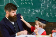 © be free - Father with beard, teacher teaches bored son, little boy. Boring studying concept. Kid fed up with studying, kicks away teacher. Teacher and pupil in mortarboard, chalkboard on background.