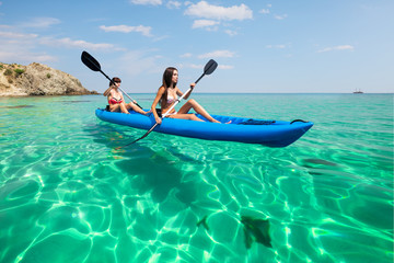 Wall Mural - Two young women kayaking in the sea. Beautiful woman canoeing on the island on a summer day.