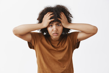 Waist-up shot of bothered and tired depressed african american woman with afro hairstyle feeling annoyed and exhausted with louds of troubles on head frowning holding hands on hair