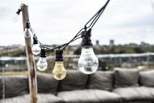 Glühbirnen an Lichterkette auf Dachterrasse über den Dächern – kaufen