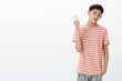 Bossy serious-looking cool young teenage asian guy in striped t-shirt taking away smartphone as being distracted. Guy turning away from cellphone not hear yell of mother as coming home late