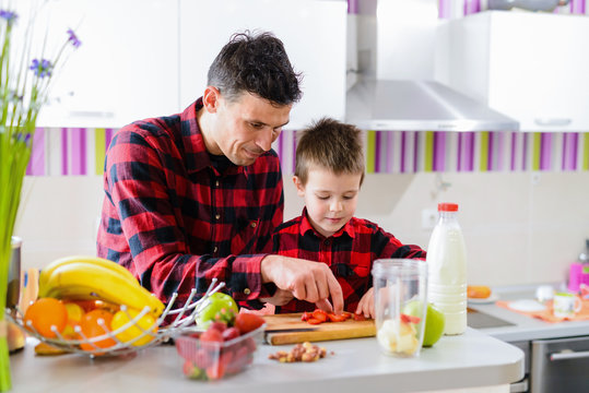 Cute father and son making healthy breakfast together. Sitting by the kitchen table full of fresh fruits.
