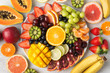 Raw fruits berries platter, mango, oranges, kiwi strawberries, blueberries grapefruit grapes, bananas apples on the white plate, on the off white table, top view, selective focus