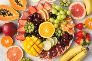 Wall Mural - Raw fruits berries platter, mango, oranges, kiwi strawberries, blueberries grapefruit grapes, bananas apples on the white plate, on the off white table, top view, selective focus