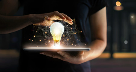  Abstract business. Human hands holding light bulb glowing on tablet and network connection communication on virtual interface, Innovation and technology concept.