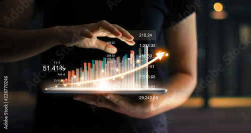 Fotografía Businessman holding tablet and showing a growing virtual hologram of statistics, graph and chart with arrow up on dark background